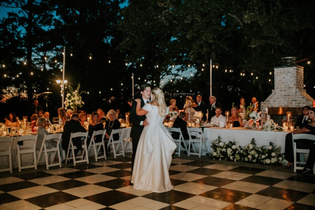 Bride and groom dancing on a checkerboard dance floor under string lights at their reception