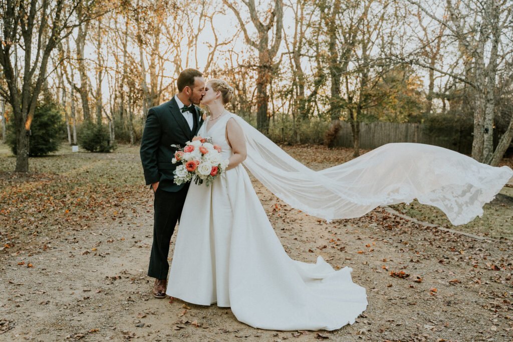 Bride and groom kissing as her veil sweeps behind them on an autumn afternoon