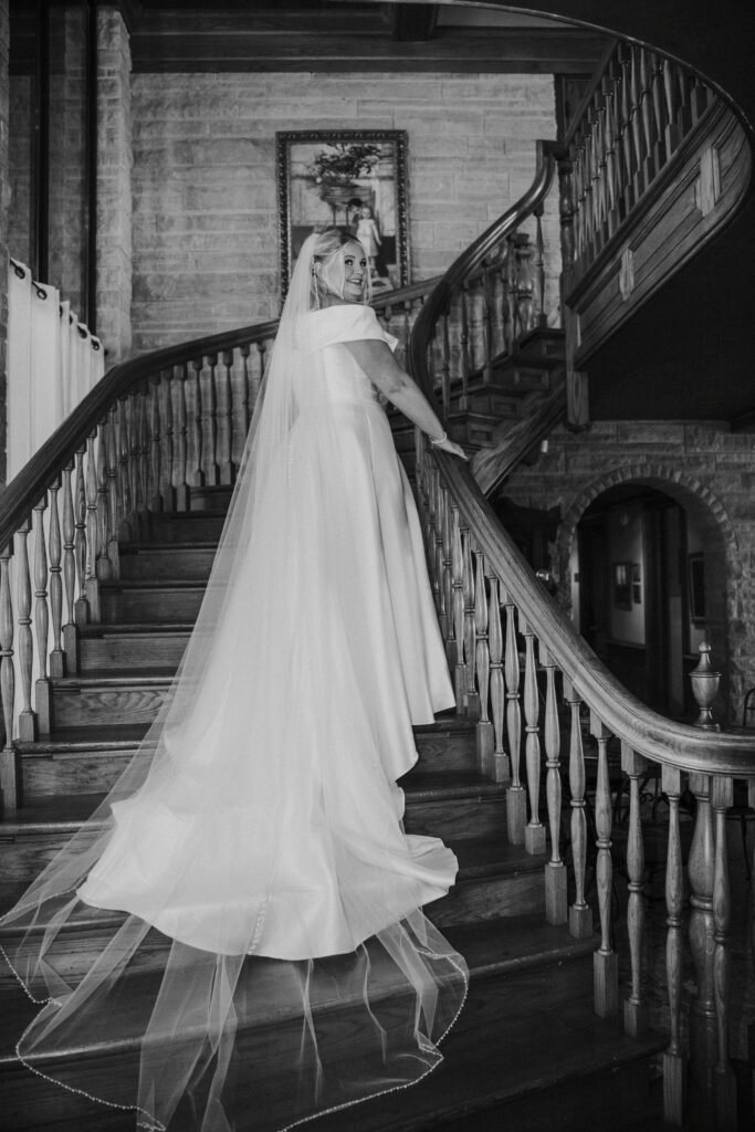 Black and white portrait of a bride with her veil spread across a grand staircase