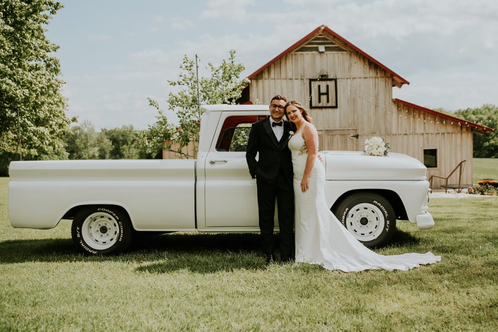 Bride and groom with a vintage truck outside the barn at Holland Barn
