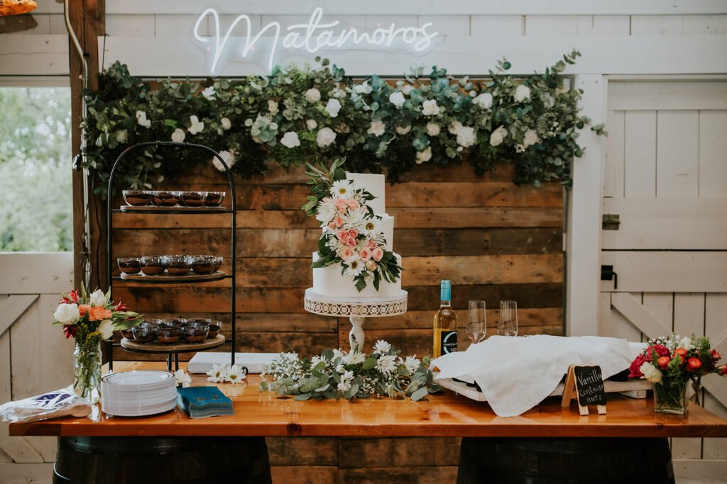 Wedding cake and dessert table against a floral backdrop at a Holland Barn reception