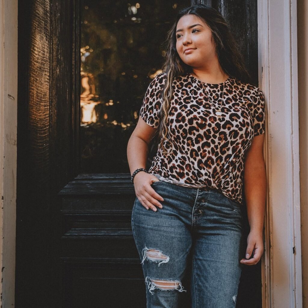 Senior girl in a leopard print top leaning in a dark doorway, downtown NWA senior pictures