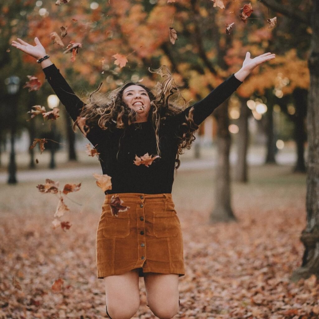 Senior girl tossing fall leaves in the air in a corduroy skirt, fall senior pictures NWA