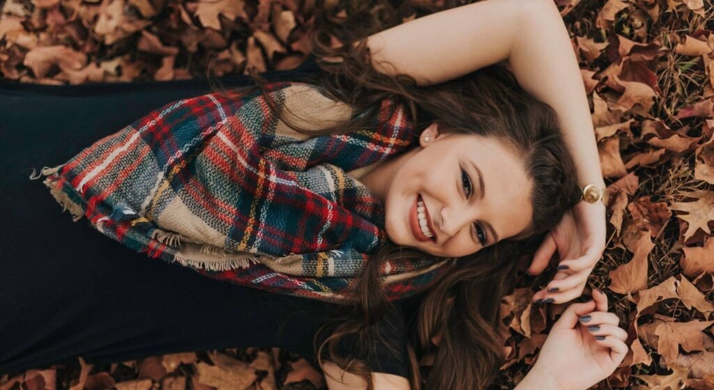 Senior girl in a plaid scarf lying in fall leaves, fall senior pictures NWA