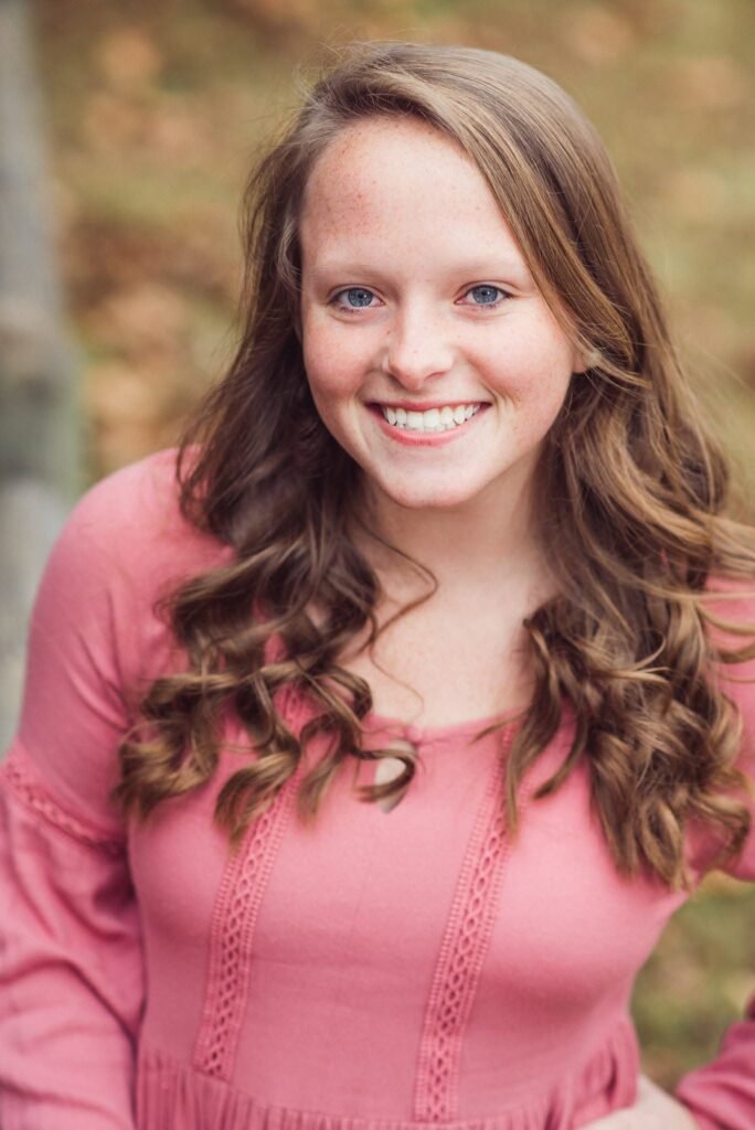 Smiling senior girl in a pink top in warm fall light, classic senior portrait NWA