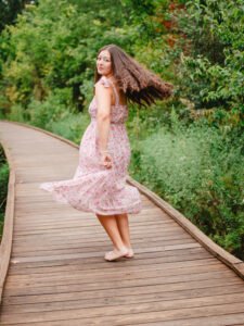 Senior girl in a pink floral dress twirling on the boardwalk at Osage Park in Bentonville, Arkansas