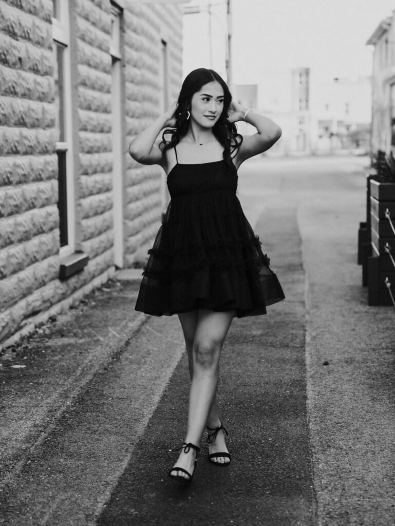 Black and white senior portrait in a black dress on a downtown sidewalk