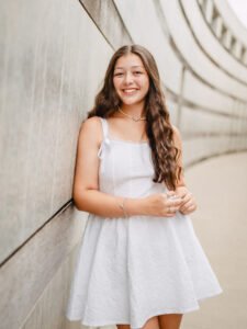 Senior girl in a white dress smiling against a curved concrete wall at Crystal Bridges, Bentonville senior portrait