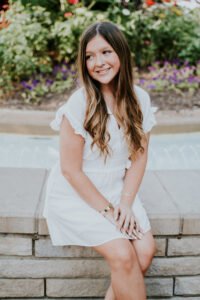 Senior girl in a white dress sitting among flowers on the Bentonville downtown square, NWA senior pictures