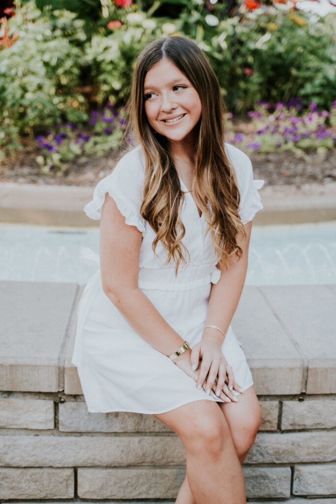 Senior girl in a white dress sitting among flowers on the Bentonville downtown square, NWA senior pictures