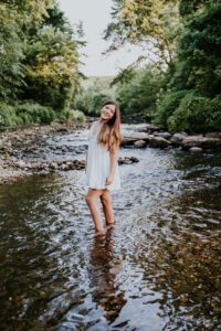 Senior girl in a white dress standing in the creek at Tanyard Creek in Bella Vista, outdoorsy NWA senior pictures