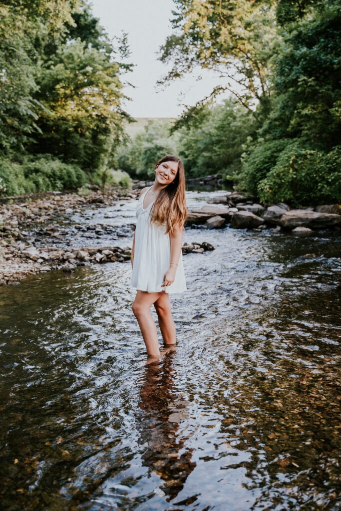 Senior girl in a white dress standing in the creek at Tanyard Creek in Bella Vista, outdoorsy NWA senior pictures