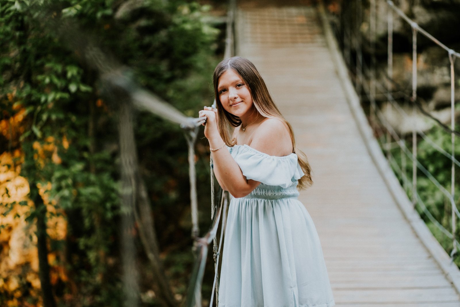 Senior girl smiling while holding the rope of the suspension bridge at Tanyard Creek in Bella Vista, NWA senior pictures