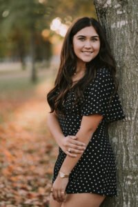 Senior girl in a polka dot romper leaning on a tree in front of Old Main at the University of Arkansas, Fayetteville senior pictures