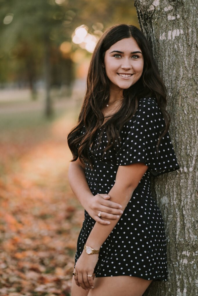 Senior girl in a polka dot romper leaning on a tree in front of Old Main at the University of Arkansas, Fayetteville senior pictures