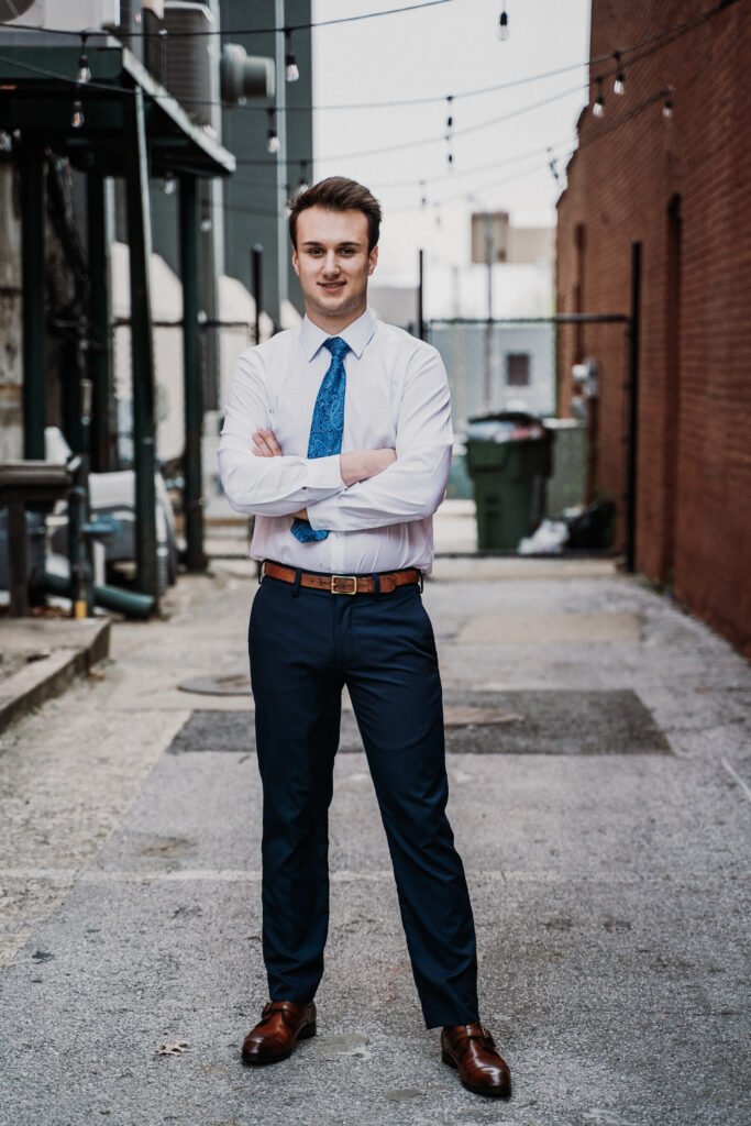 Senior guy in a white button-down, blue tie and navy pants in a downtown alley, NWA senior pictures