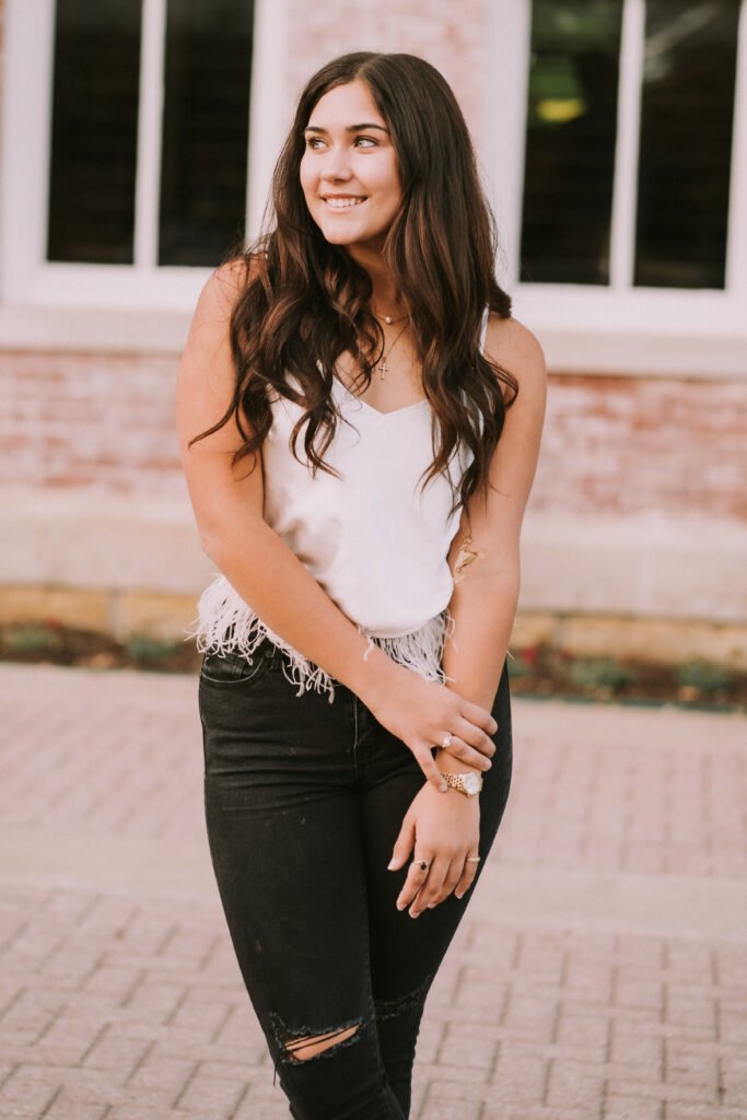 Senior in a white top and black jeans by the brick walls of Old Main