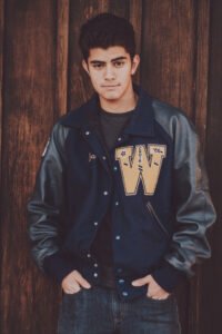 Senior guy in a letterman jacket against a wooden wall on Emma Avenue in downtown Springdale, Arkansas