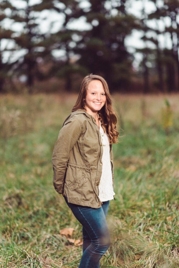Senior in an olive jacket in a grassy field at Gulley Park
