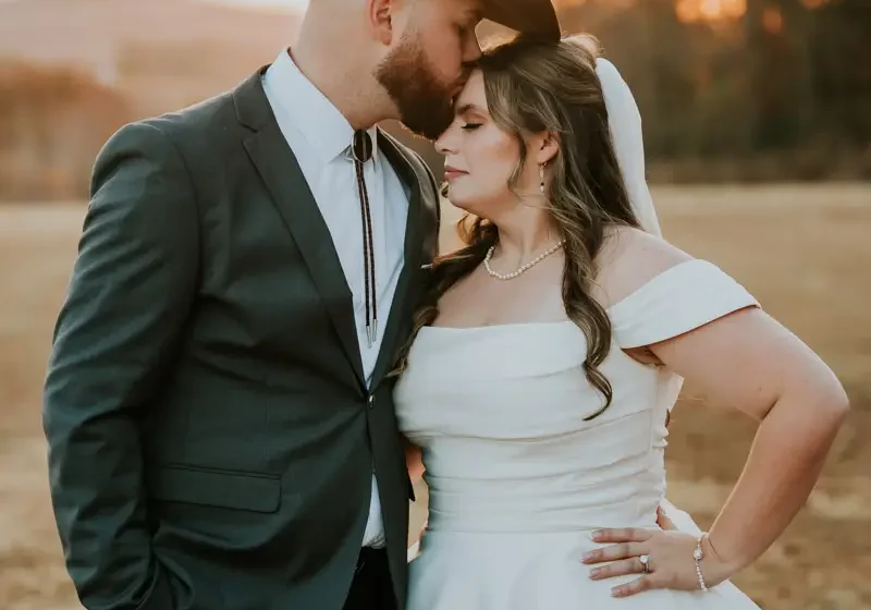 Groom in a grey suit kissing his bride outdoors