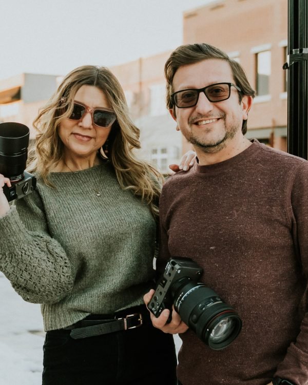 Randy and Olga of Haziel Photo & Films holding their cameras on a street in downtown Bentonville, Arkansas