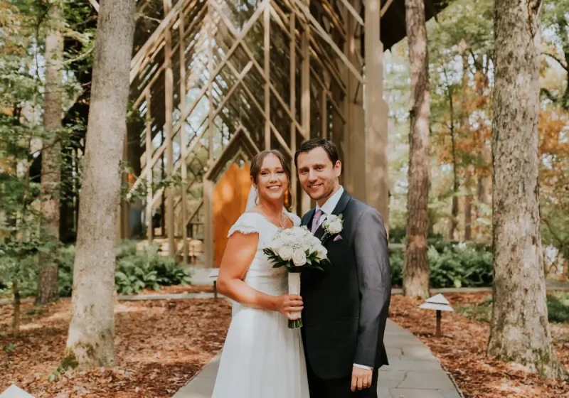 Bride and groom standing among tall trees, bride holding her bouquet