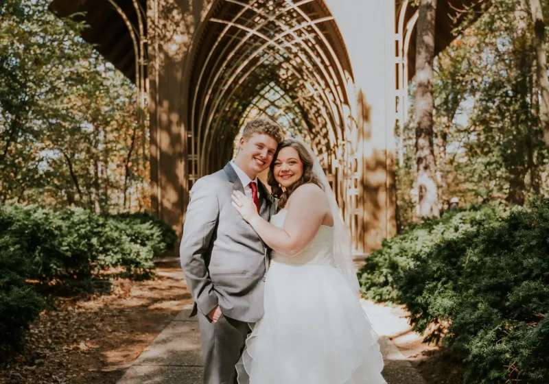 Bride and groom embrace under the stone arches at Thorncrown-style glass chapel in Northwest Arkansas