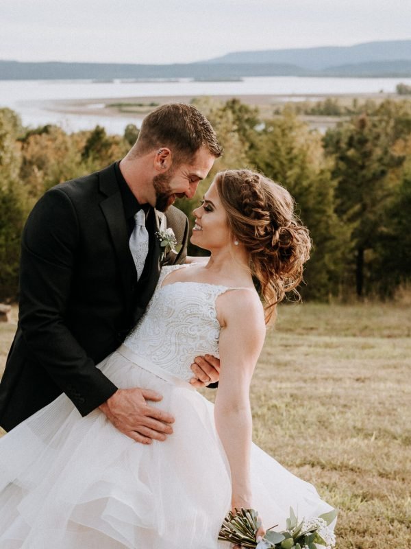 Groom holds his bride close in an open field at a Northwest Arkansas wedding